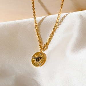 Detalle del colgante ovalado dorado con abeja y estrella sobre tela de seda