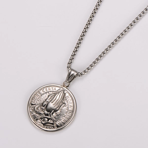 Macro detail of silver stainless steel prayer hands pendant with Latin engraving