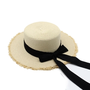 Detail of raffia straw hat featuring a flat top, frayed edges, and a black ribbon bow