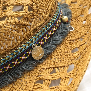 Detail of woven straw cowboy hat featuring ethnic ribbon, grey fringe, and gold coin charm