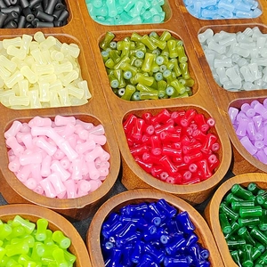 Close-up of bamboo-shaped faux jade glass beads in a wooden tray with various colors