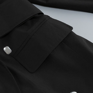 Détail d'une robe noire montrant une poche à rabat avec bouton en cristal brillant