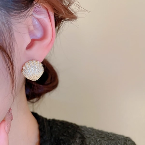 Macro detail of shell-shaped gold earrings with zircon pavé worn by a model