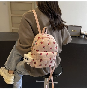 Detailed close-up of pink corduroy backpack with red strawberry prints and plush keychain