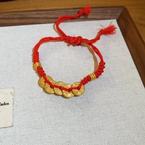 Detail of red braided cord bracelet with five lucky golden coins and metal beads