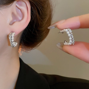 Detail of silver C-shaped earrings with double rows of white pearls and sparkling rhinestones