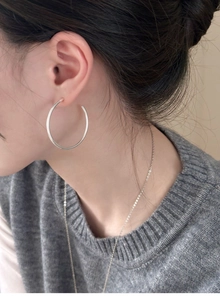 Side view of large silver-colored C-shaped hoop earrings worn by a model in natural light