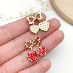 Close-up of a small heart-shaped red cherry pendant with rhinestones on a finger