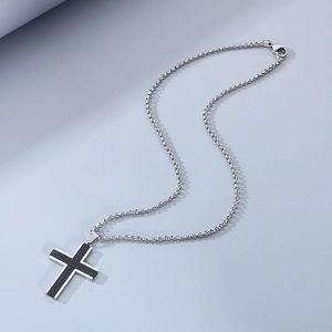 Close-up of a silver cross pendant with black matte texture on a steel chain