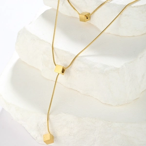 Detail of a golden Y-shaped snake chain necklace with small cubic pendants on white stone