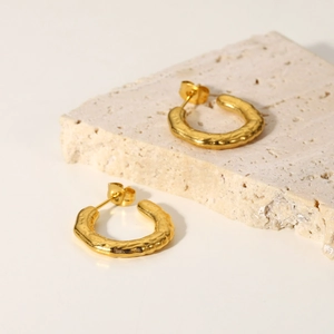 Macro shot of 18K gold plated stainless steel lava-effect C-shape earrings on stone