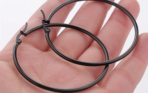 Detailed view of large matte black hoop earrings held in hand for scale comparison