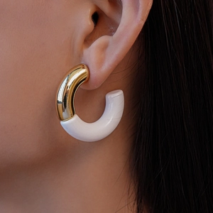 Close-up of a two-tone C-shaped hoop earring in gold metal and white resin on a model