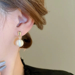 Gros plan de boucles d'oreilles en perles dorées portées par un mannequin sous lumière douce