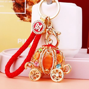 Close-up of golden pumpkin carriage keychain with rhinestones and red braided cord