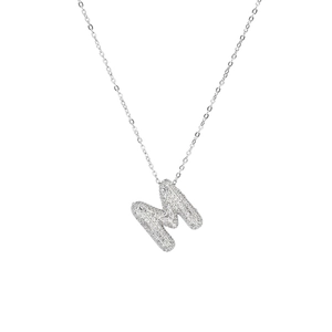 Macro shot of silver letter M pendant encrusted with white zircon stones on white background