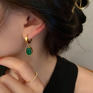 Macro shot of titanium steel emerald earrings on model with gold vintage jewelry
