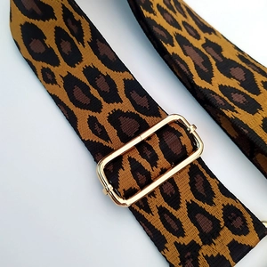 Detail of adjustable leopard print bag strap with golden metal buckle and woven texture
