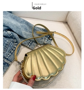 Detail einer goldenen Muschel-Handtasche mit eleganter Perlenkette und Lederriemen