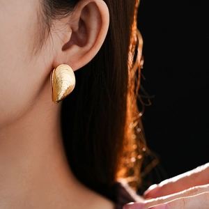 Close-up of elegant gold shell-shaped threaded earrings worn by a model in detail