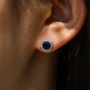 Close-up of a blue zircon halo stud earring worn on ear with sparkling white crystals