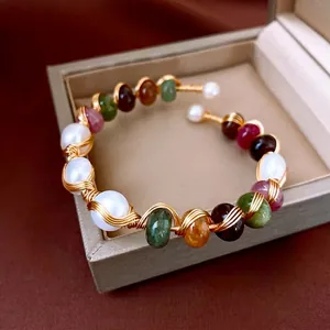 Handcrafted gold wire open bangle with natural agate and pearls on a display case