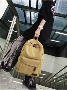 Detail of khaki canvas backpack featuring front zipper pocket and brown leather accents