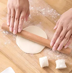 Solid wood rolling pin being used for dumpling dough on a wooden board with flour