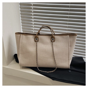 Detail of beige canvas tote bag with brown leather trim and metal chain strap
