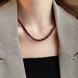 Detail of deep red gemstone chip necklace worn by a model in a professional office blazer