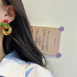 Detail of beaded Christmas wreath earrings with red bow shown on a person's ear