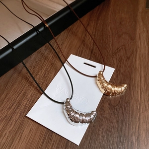 Macro shot of gold and silver croissant pendants with realistic pleated textures on leather cords