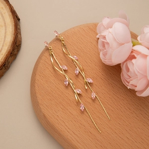 Elegant gold leaf tassel earrings with pink marquise gems on a minimalist wooden tray
