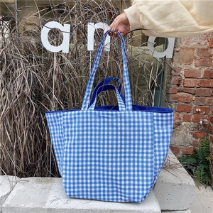 Detail of blue and white checkered tote bag with durable fabric handles in outdoor setting