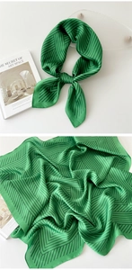 Detail of green silk scarf with black geometric lines tied and laid flat on white surface