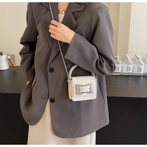 Close-up of cream mini crossbody bag featuring a bold silver buckle and chain strap