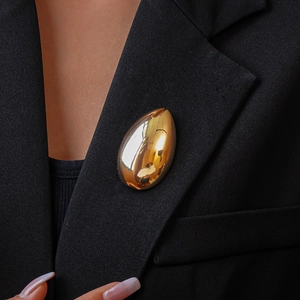 Close-up of a polished gold metallic teardrop brooch pinned to a black suit lapel