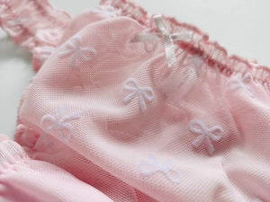 Detail of pink mesh fabric with white bow patterns and a delicate satin ribbon bow