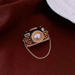 Vintage camera brooch with zircon, pearl, and black enamel on a luxury velvet background