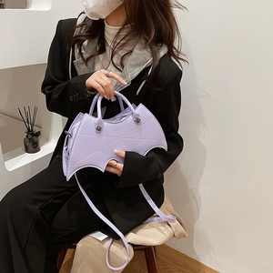 Model wearing a lilac bat-shaped leather handbag with crossbody strap in a studio setting