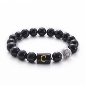 Detail view of black onyx and white turquoise beads with a golden letter C charm bracelet