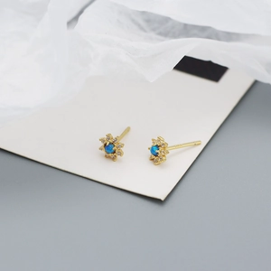 Macro shot of gold daisy stud earrings with central blue gemstone and pavé zircon details