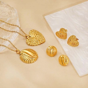 Golden stainless steel jewelry set featuring heart and shell pendants on silk texture
