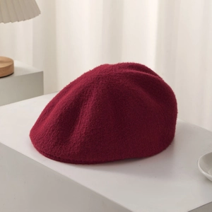 Detailed texture of burgundy wool beret with metal logo emblem on clean background