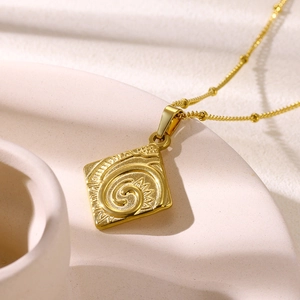 Macro detail of square gold pendant with spiral engraving on elegant bead chain necklace