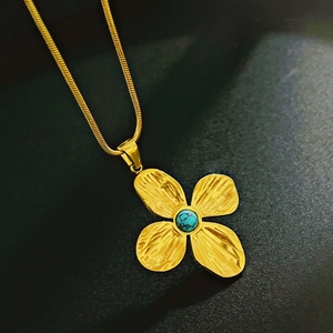 Close-up of gold flower necklace with turquoise inlay on a black textured surface