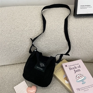 Détail du mini sac seau en velours côtelé noir avec écusson logo sur surface texturée