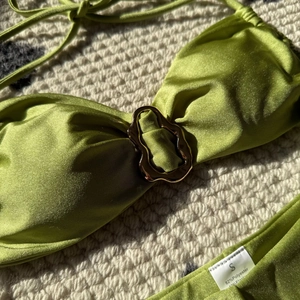 Detail eines olivgrünen Bikinis mit glänzendem Satinstoff und goldenem Ringverschluss