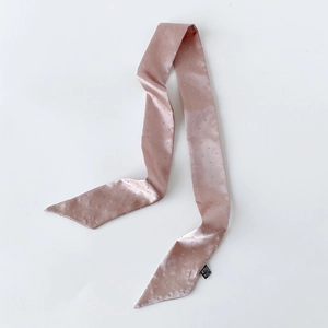 Detail eines rosa Satin-Seidenschals mit silbernen Ziernieten und schwarzem Etikett auf Weiß