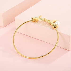 Detailed view of golden adjustable bracelet with airplane, cross disk, and pearl charms